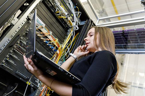 Woman network technician performing diagnostic Managed IT services with a laptop and working with support in front of network switches within the datacenter server rack for Northwest Techies in McMinnville Salem and Portland Oregon